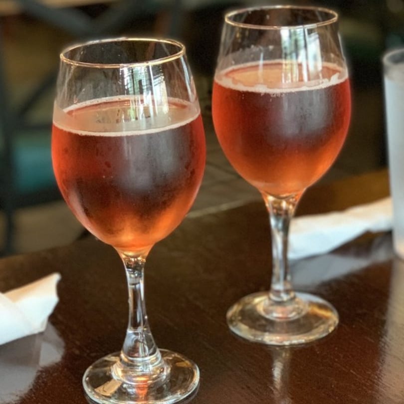 Two glasses of chilled rosé wine with condensation on a dark wooden table at White Wolf Cafe.