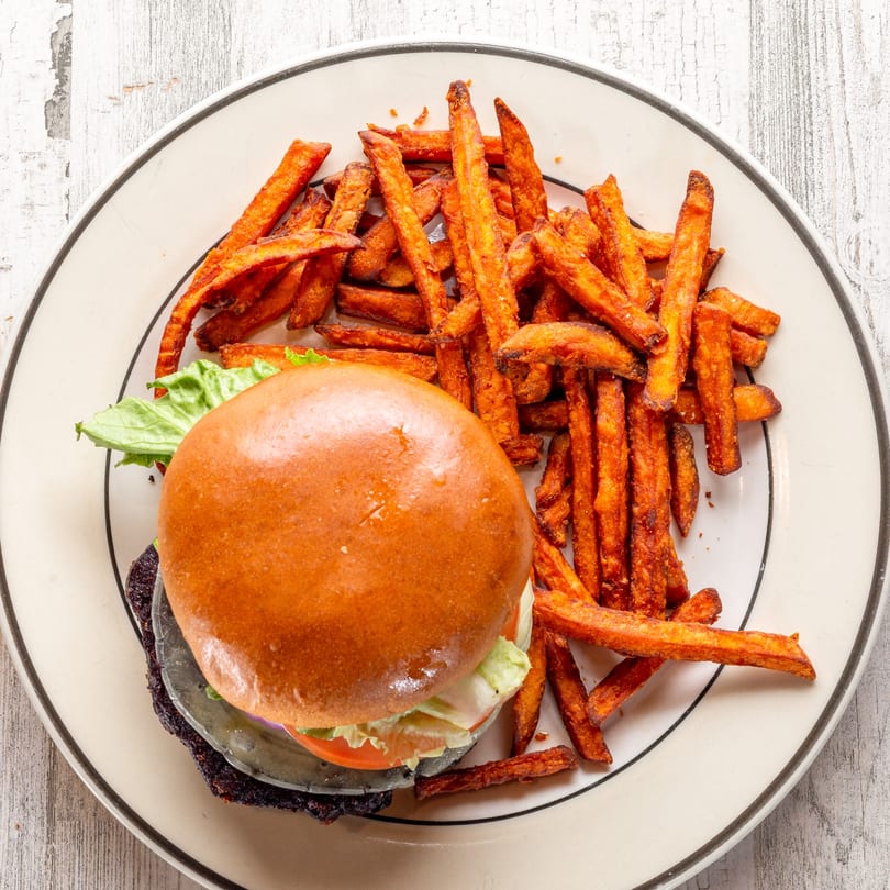 A White Wolf Cafe veggie burger with lettuce, tomato, and sweet potato fries on a white plate.