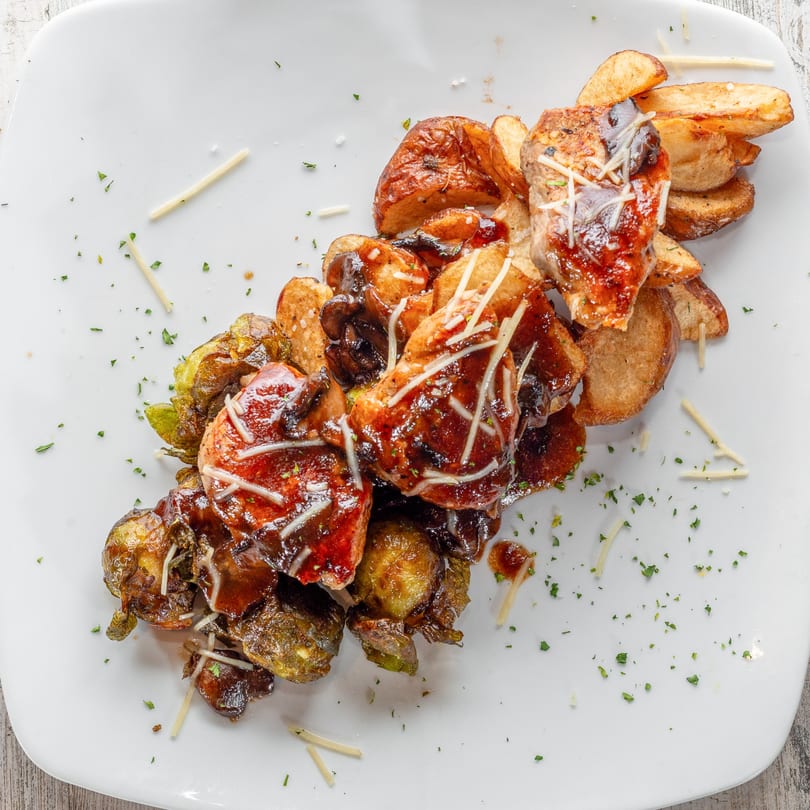 White Wolf Cafe's chicken and roasted brussels sprouts with potato wedges, drizzled with sauce and cheese.