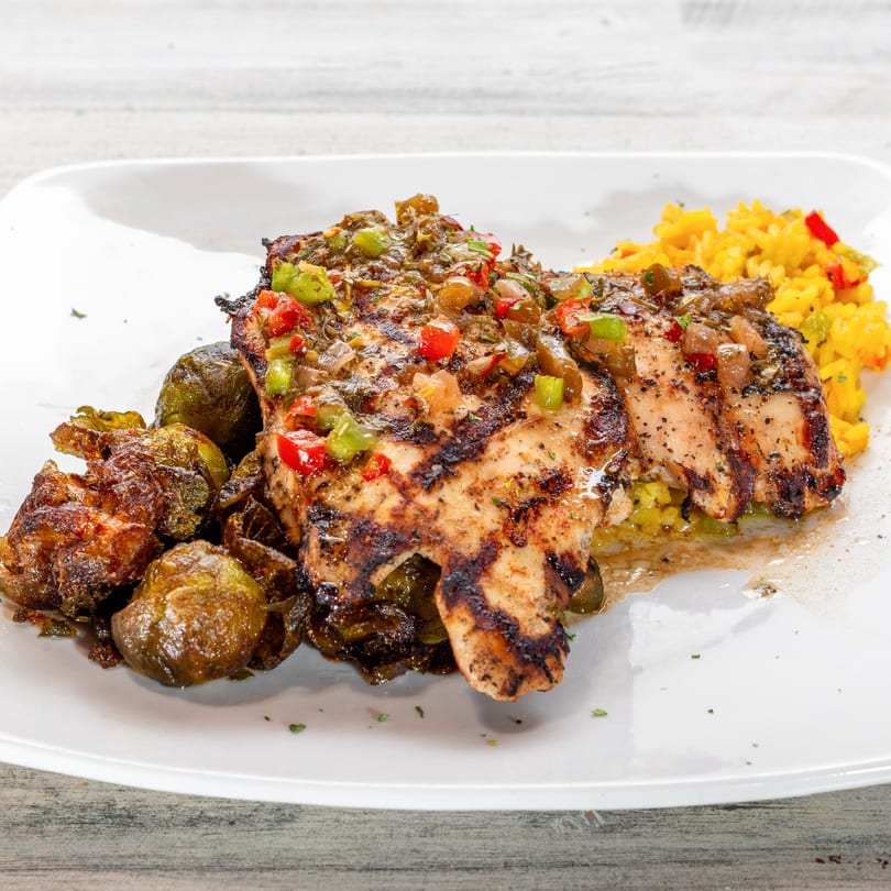 Grilled chicken with colorful salsa, roasted Brussels sprouts, and yellow rice on a white plate.