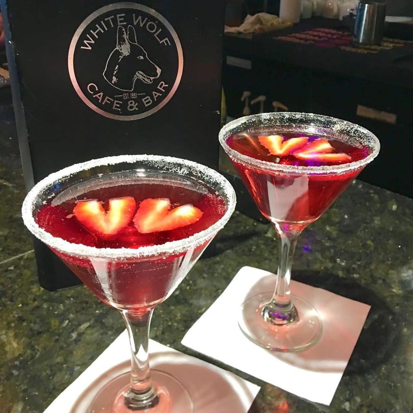 Two red cocktails with strawberry slices and sugar-rimmed glasses on a bar at White Wolf Cafe.