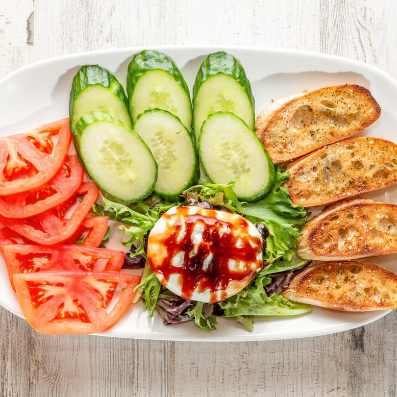 A White Wolf Cafe Caprese salad with sliced tomatoes, cucumbers, mozzarella, and toasted bread.