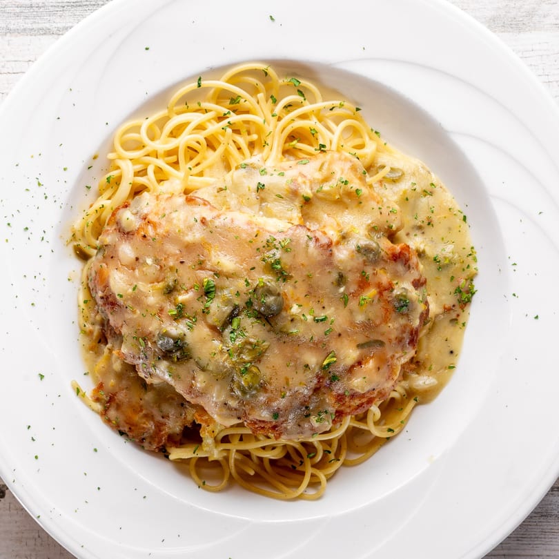 Chicken piccata with capers and creamy sauce over spaghetti, garnished with parsley at White Wolf Cafe.